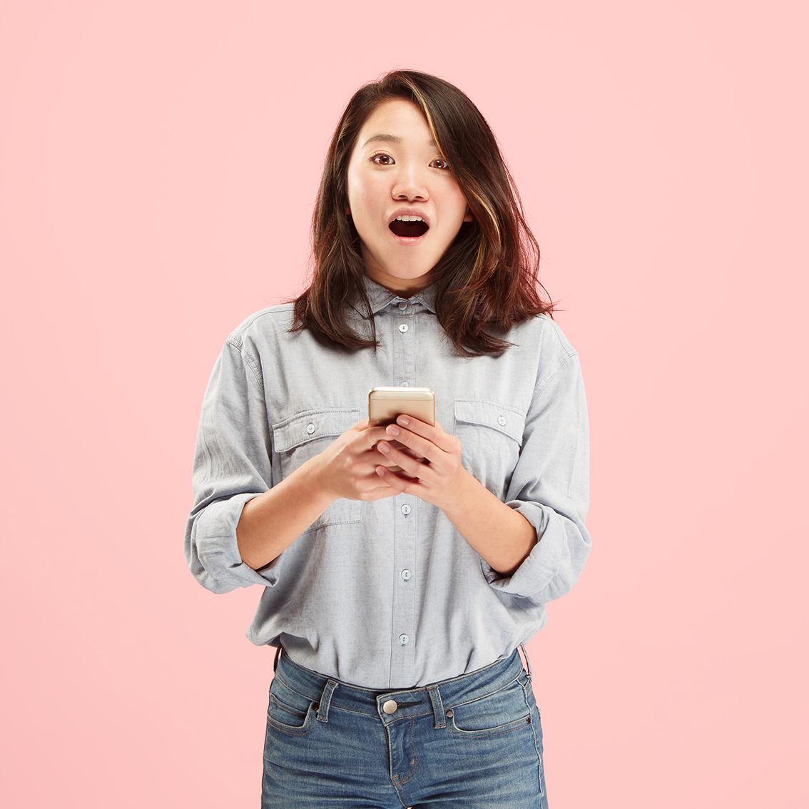 Young woman in a canadian tuxedo with shoulder length brown hair holding her smart phone with an excited expression.