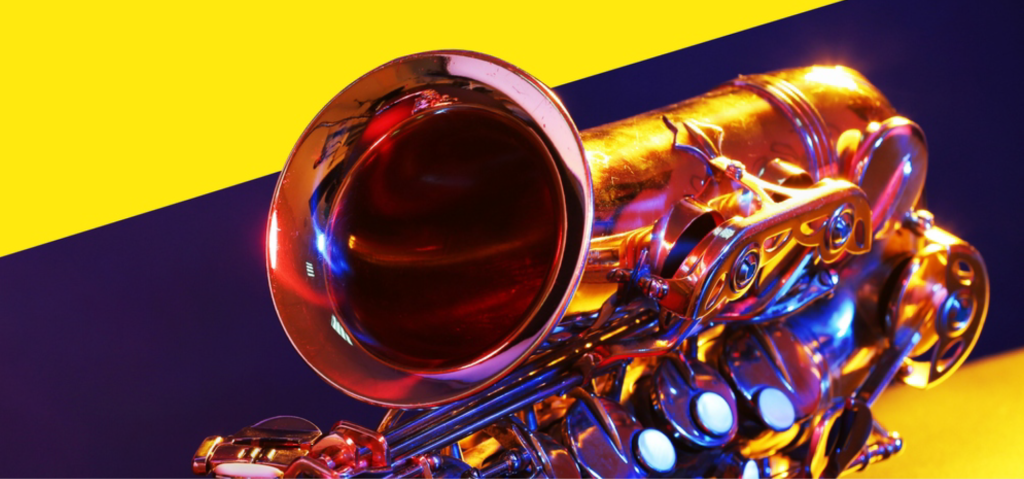 Close up image of a saxophone on its side with the purple and yellow background reflecting off of it's shiny surface.